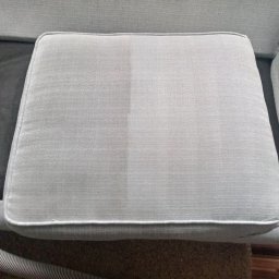 Łowcy Porządku - Firma Sprzątająca - Jasnoszary poduszka kanapy w trakcie czyszczenia, widoczna wyraźna różnica między wyczyszczoną a brudną częścią, obok dysza odkurzacza piorącego.