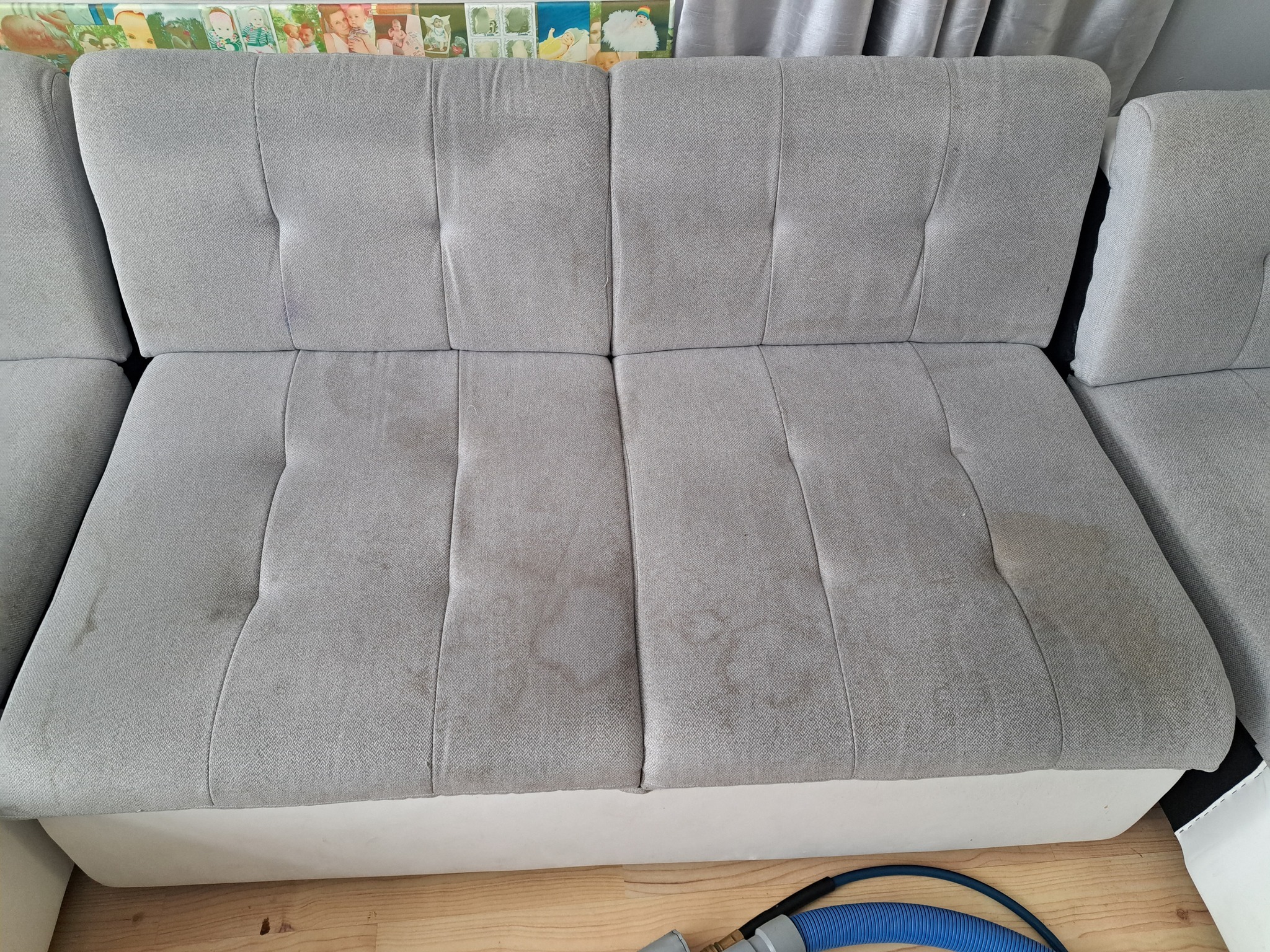 Szara kanapa z widocznymi plamami na siedzisku przed czyszczeniem, widoczny fragment węża odkurzacza piorącego.