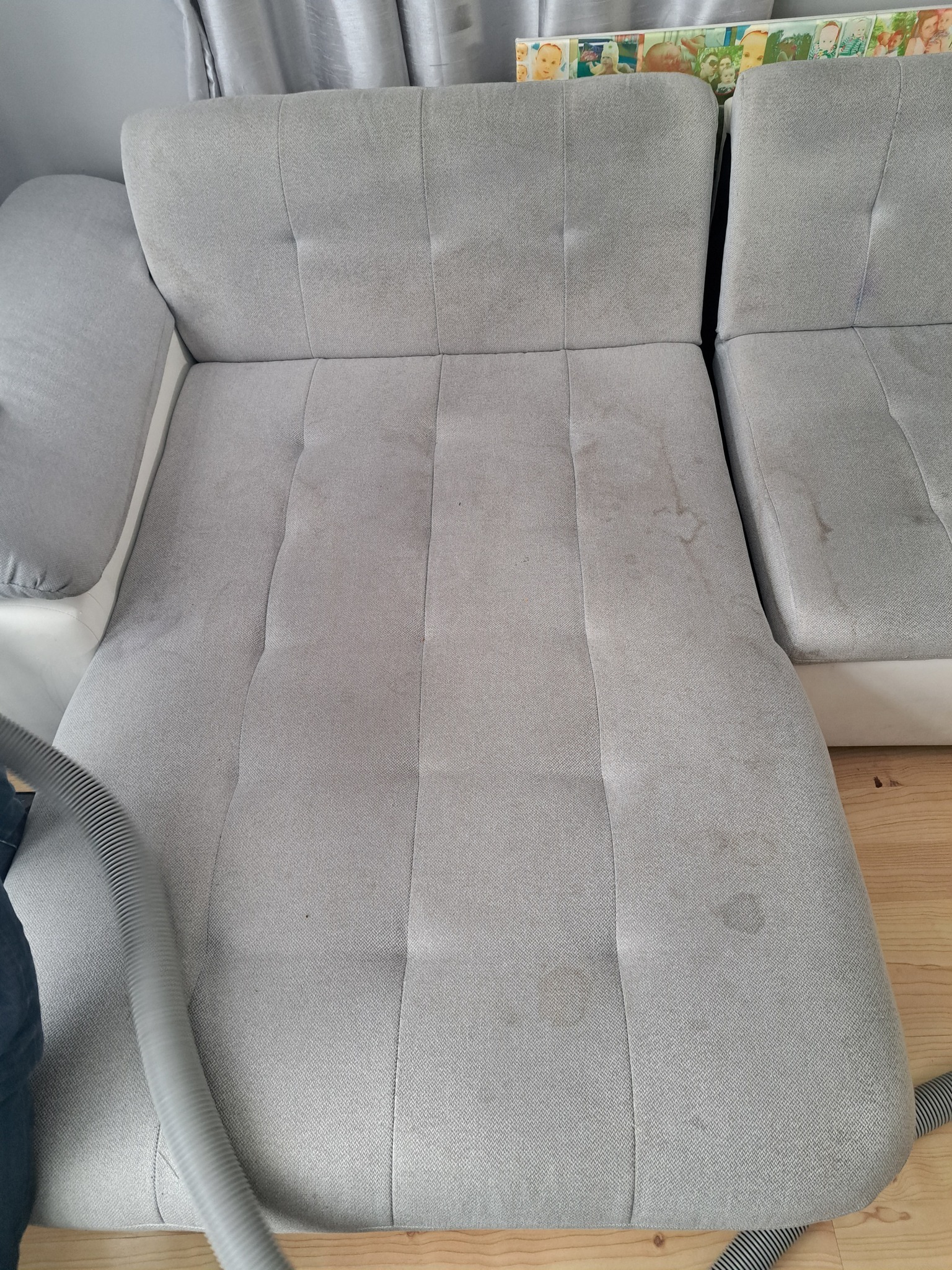 Szara, modułowa kanapa z widocznymi plamami na siedzisku, czyszczona za pomocą odkurzacza piorącego z szarą rurą.