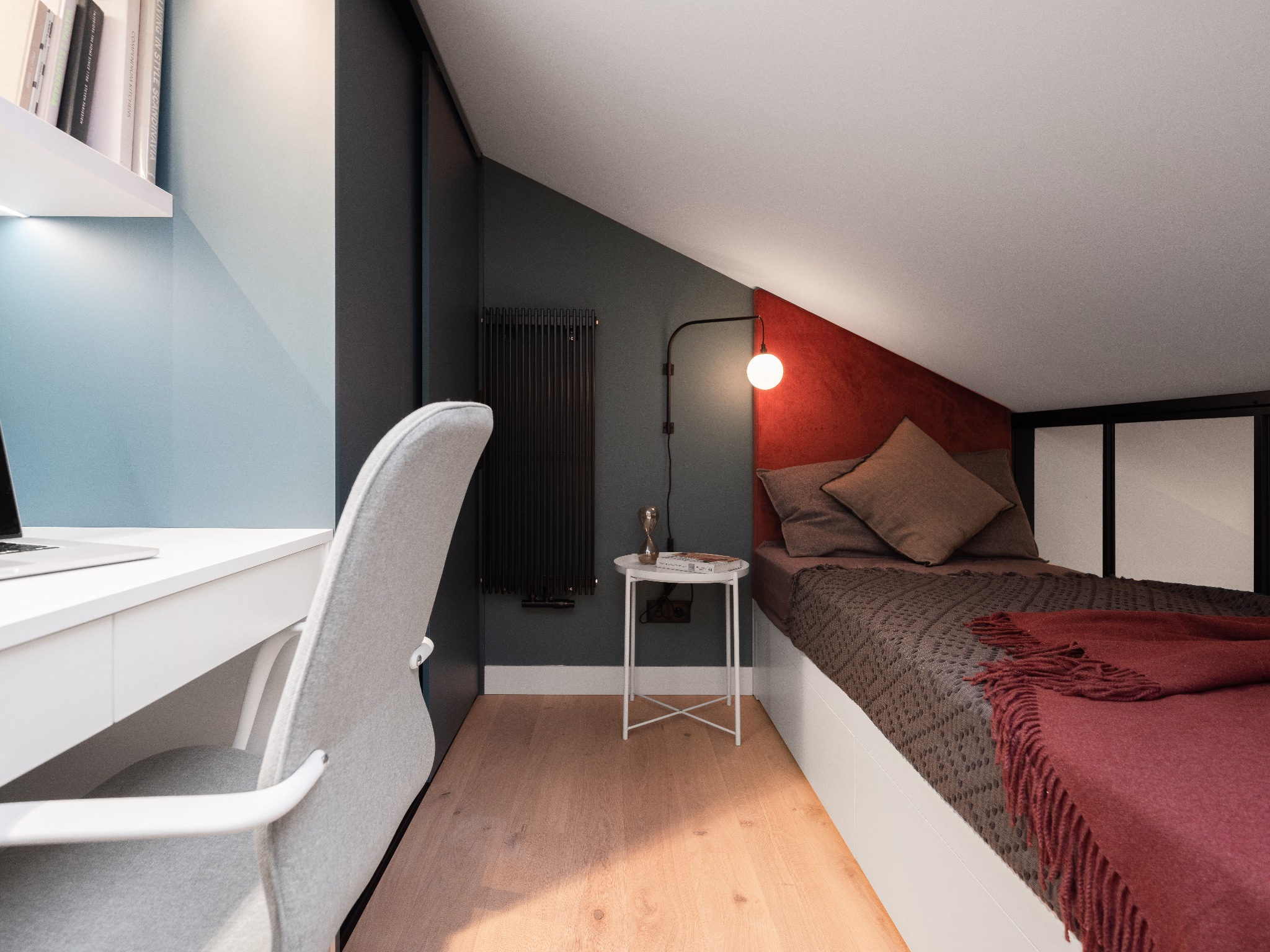 Pokój na poddaszu z biurkiem i łóżkiem, ściany pomalowane na niebiesko i ciemnoszaro, z elementami dekoracyjnymi w kolorze bordo.