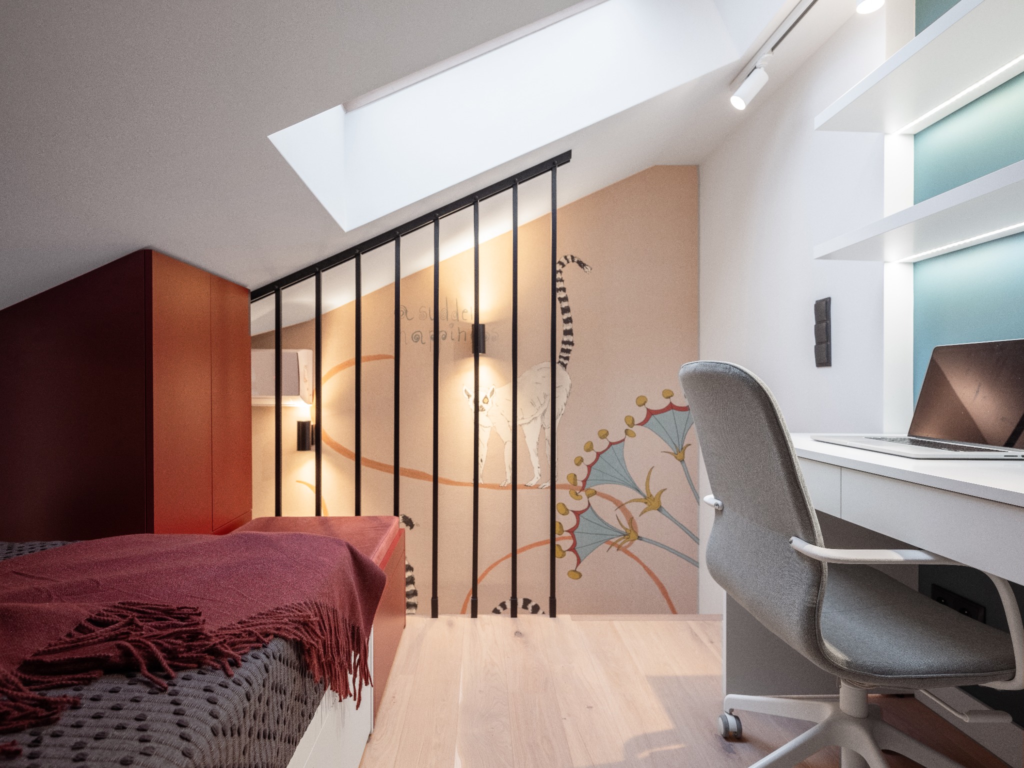 Pokój na poddaszu z łóżkiem, biurkiem i ścianą ozdobioną malowidłem przedstawiającym lemura i abstrakcyjne motywy roślinne, oświetlony przez okno dachowe i lampy punktowe.