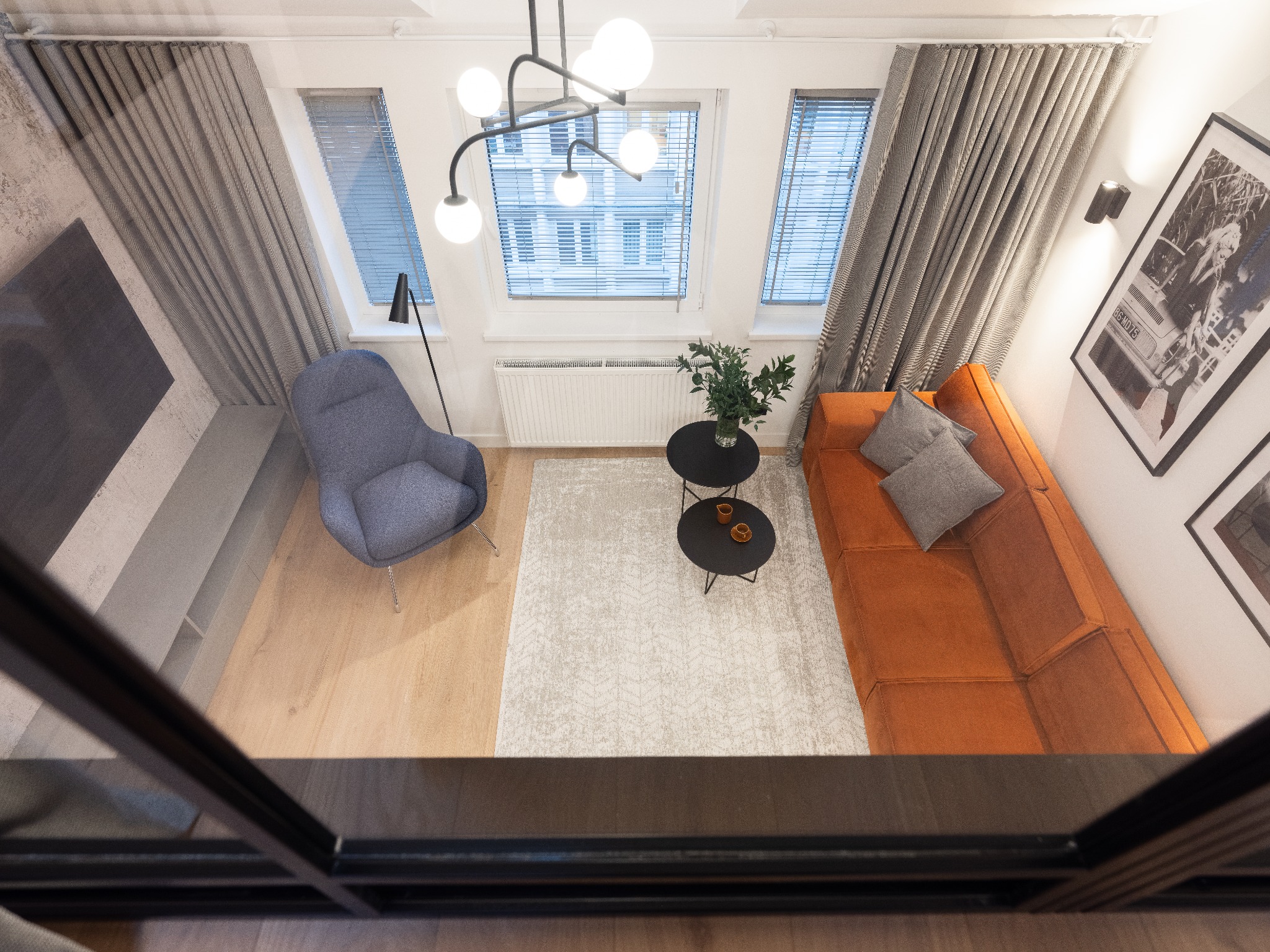 Widok z góry na jasne wnętrze pokoju dziennego z pomarańczową sofą, szarą ścianą z telewizorem i designerską lampą sufitową.