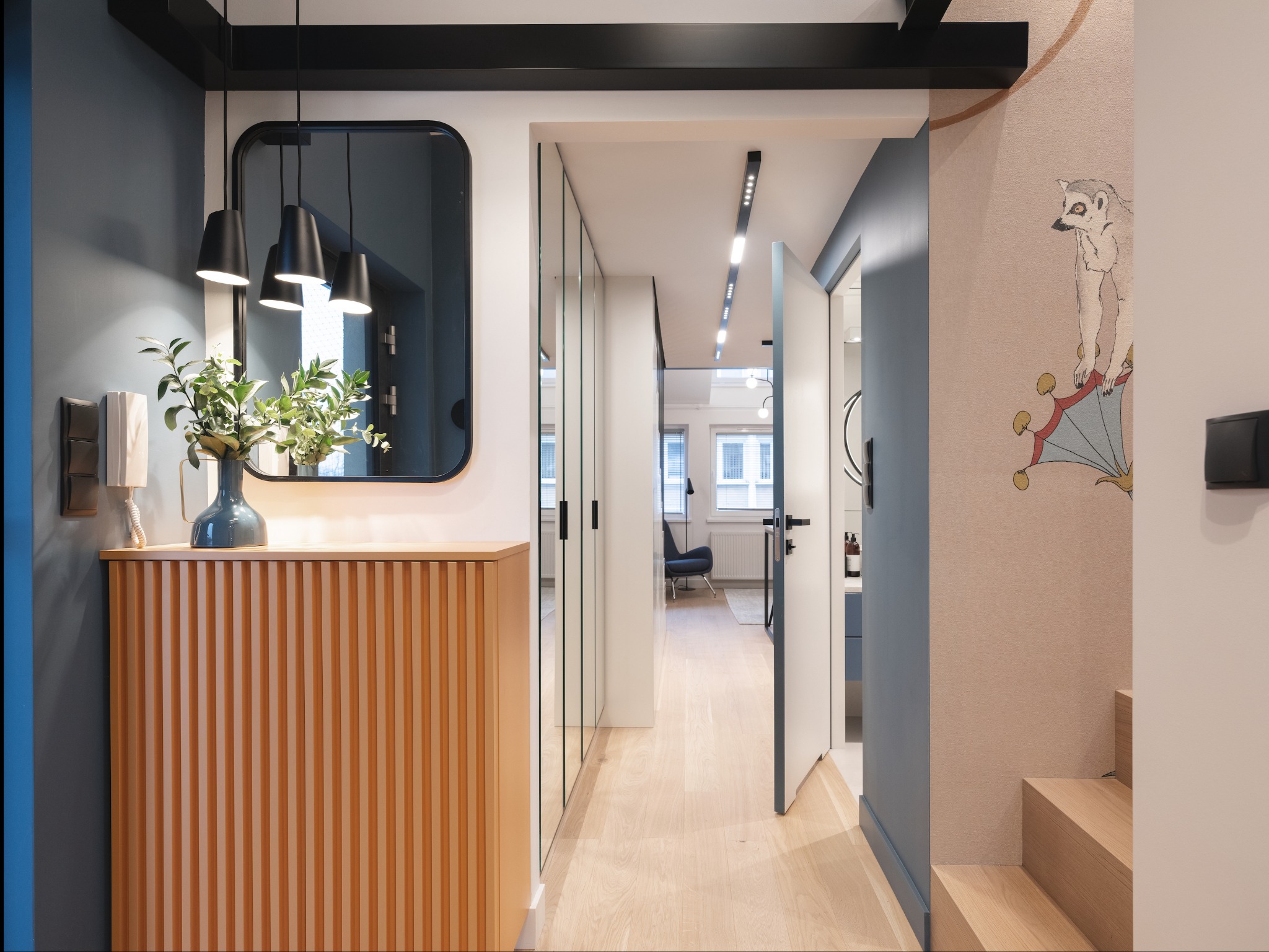 Nowoczesne wnętrze w Krakowie: przedpokój z drewnianą komodą, lustrem z oświetleniem i tapetą z motywem zwierzęcym, prowadzący do jasnego korytarza z lustrzanymi szafami.