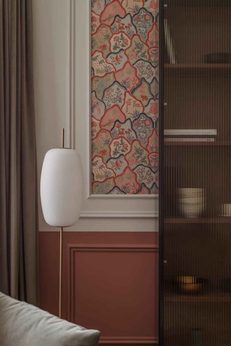 Fragment wnętrza z dekoracyjną tapetą w odcieniach czerwieni i szarości, białą lampą podłogową i przeszkloną witryną z ryflowanymi szybami.