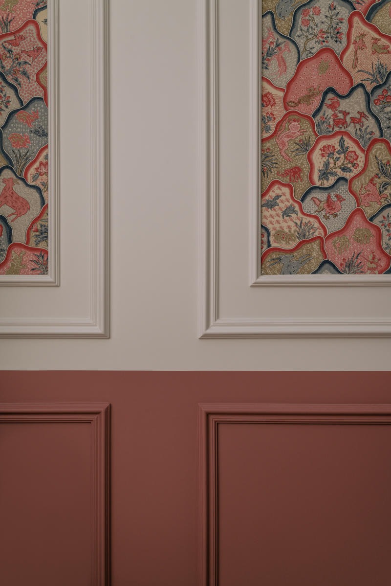 Fragment ściany w Krakowie z dekoracyjnym malowaniem w dwóch odcieniach i ozdobnym wzorzystym panelem tapetowym z motywami zwierzęcymi.