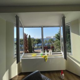 Bez Brudu 24 Dmytro Tymoshenko - Otwarty okno z widokiem na zieleń w Bydgoszczy, środki czystości i żółte ściereczki na parapecie, butelka ze spryskiwaczem na podłodze.