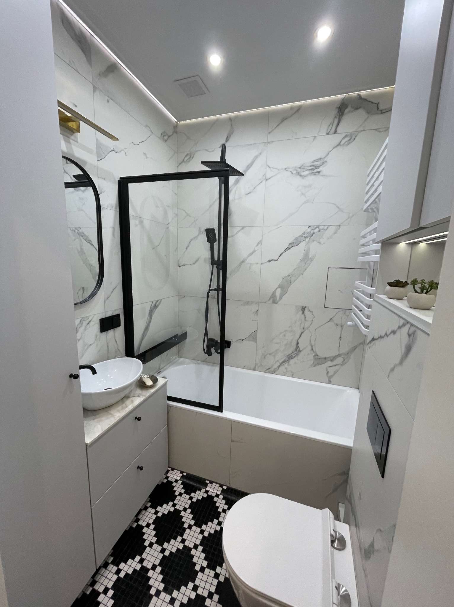 Nowoczesna łazienka z marmurowymi płytkami, czarną armaturą i geometryczną mozaiką na podłodze. Kabina prysznicowa z czarną ramą i deszczownicą. Biała umywalka nablatowa na szafce z szufladami.