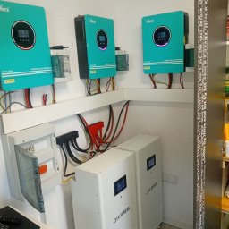 Klaudia Grzesik L-KG Instalacje Elektryczne - Kompletna instalacja fotowoltaiczna w pomieszczeniu: dwa białe magazyny energii JKESS, trzy turkusowe inwertery Ahern ECO-6200 i ECO-4200, oraz skrzynka elektryczna.