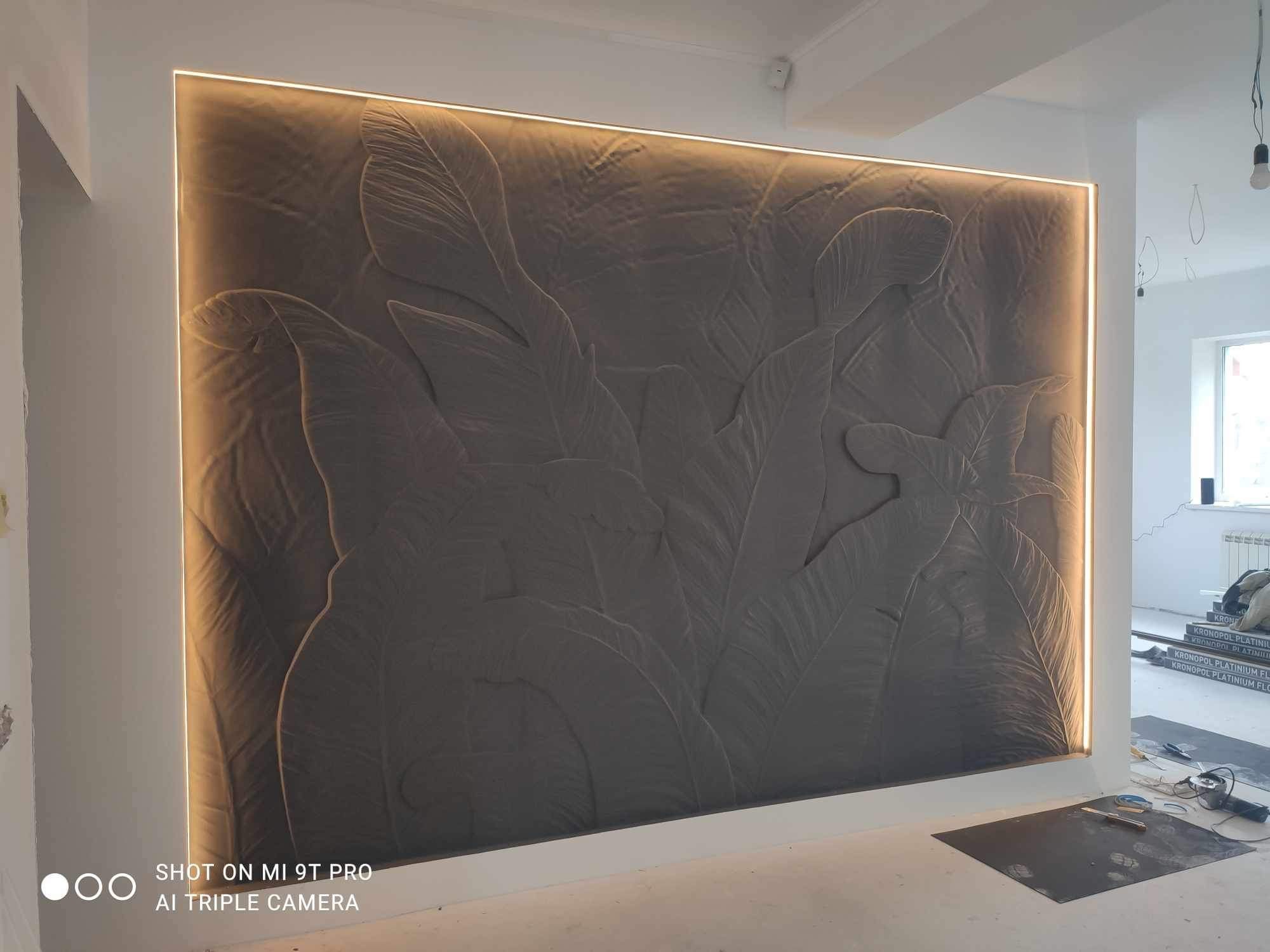 Szara ściana z trójwymiarowym wzorem liści, podświetlona paskiem LED, w trakcie prac wykończeniowych, widoczne materiały i narzędzia na podłodze.