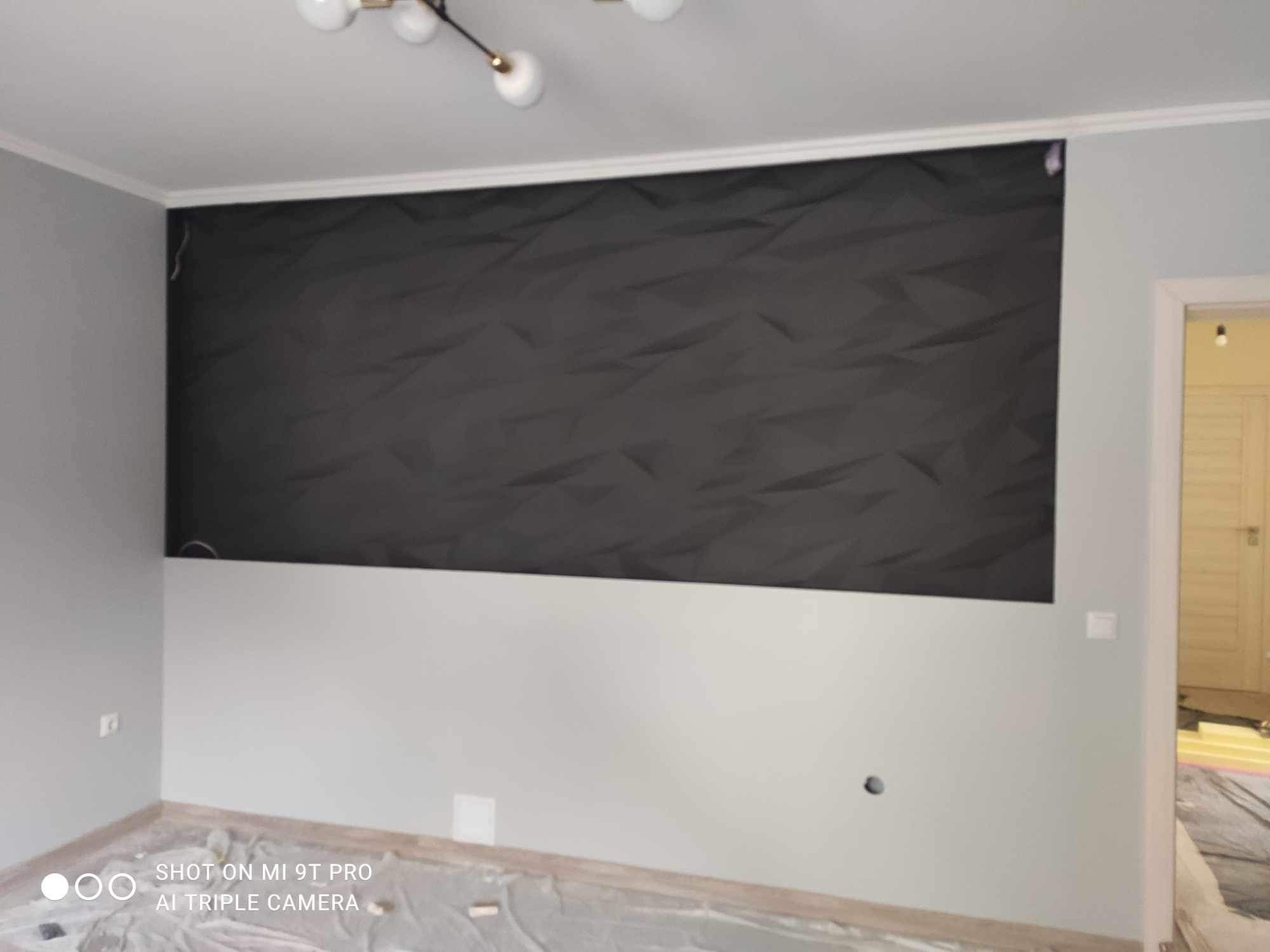Częściowo pomalowana ściana z dekoracyjnym panelem 3D w kolorze grafitowym, dolna część ściany w kolorze jasnoszarym, podłoga zabezpieczona folią malarską.