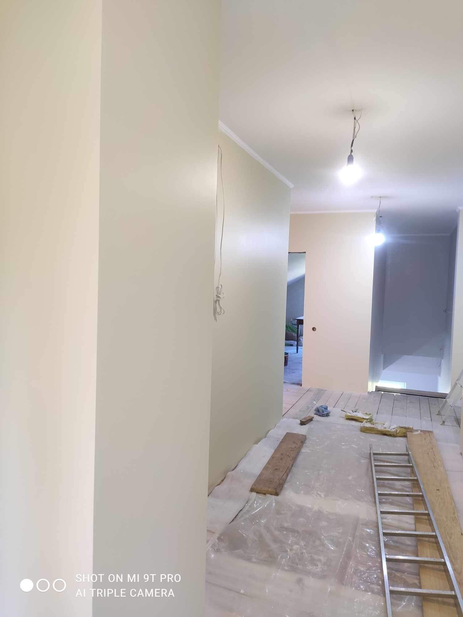 Świeżo pomalowane ściany na kremowo w korytarzu, zabezpieczona podłoga folią, widoczna drabina i narzędzia malarskie, surowy stan po malowaniu.