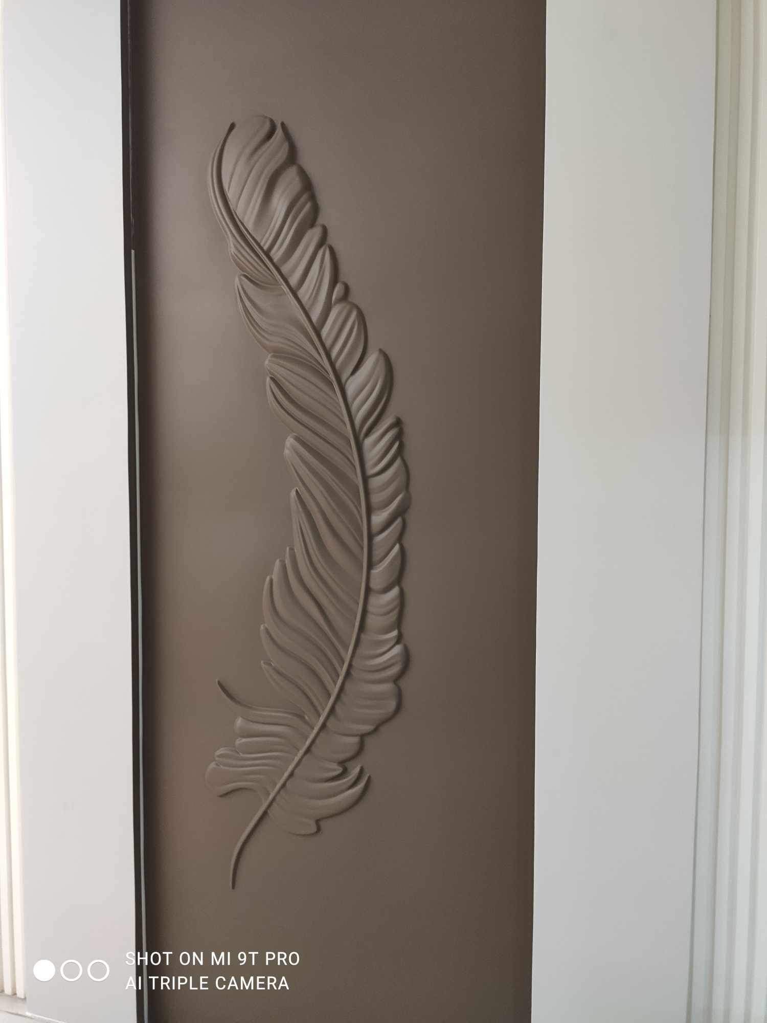 Detal dekoracyjny w postaci wytłoczonego pióra na brązowych drzwiach z białymi ościeżnicami, wykonany z gładzi.