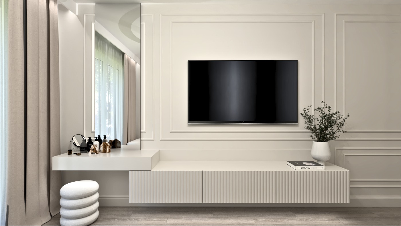 Elegancka, beżowa sypialnia z toaletką, lustrem, telewizorem i dekoracyjną ścianą z listwami. Na toaletce kosmetyki i kamienne siedzisko, pod telewizorem szafka RTV z książką Chanel i kwiatami.