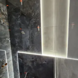 Ściana w trakcie układania płytek imitujących marmur, z podświetleniem LED w fugach i systemem poziomowania płytek.