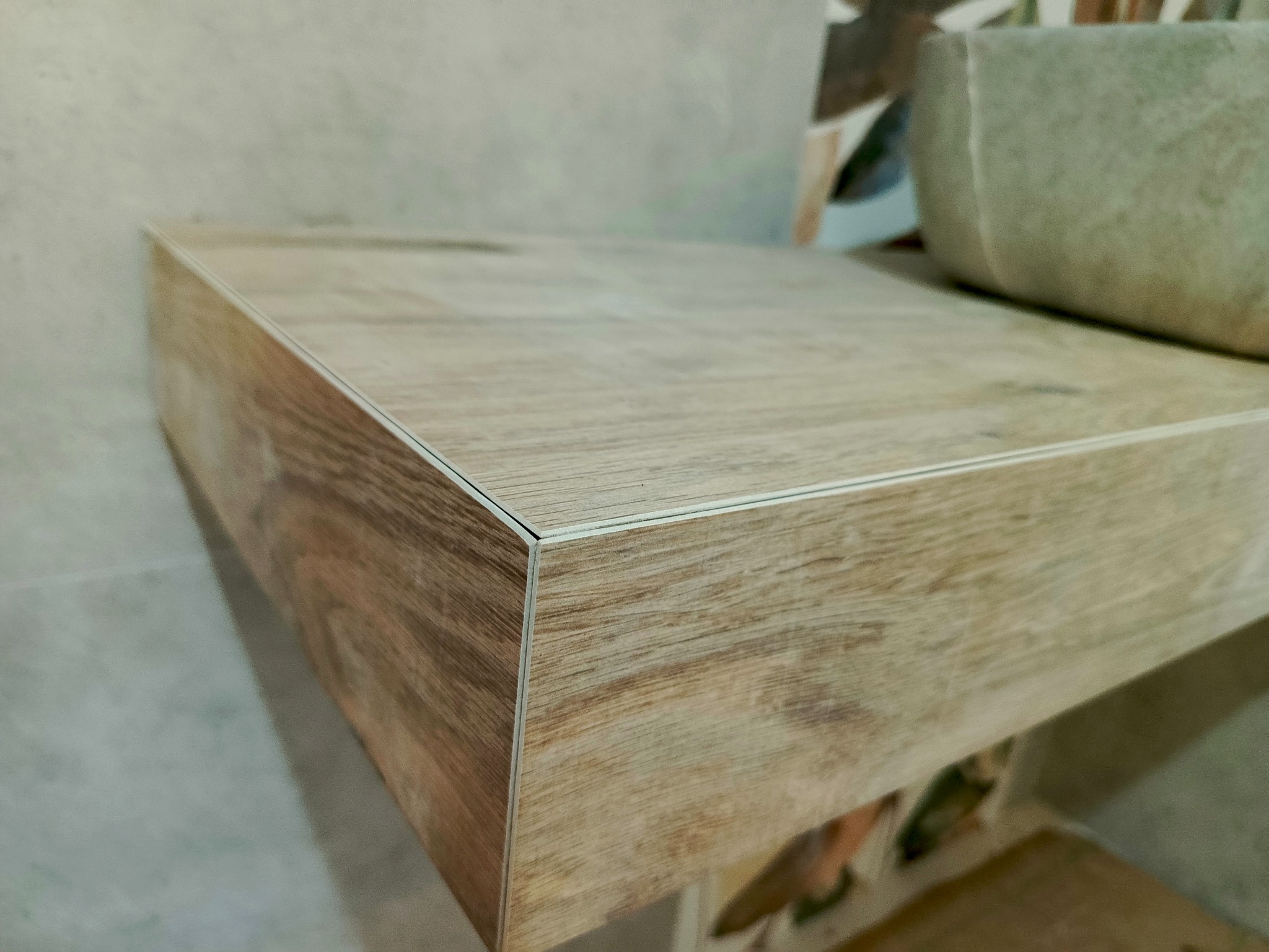 Blat łazienkowy z płytek imitujących drewno, z widocznym narożnikiem wykończonym listwą, umywalka nablatowa w tle.