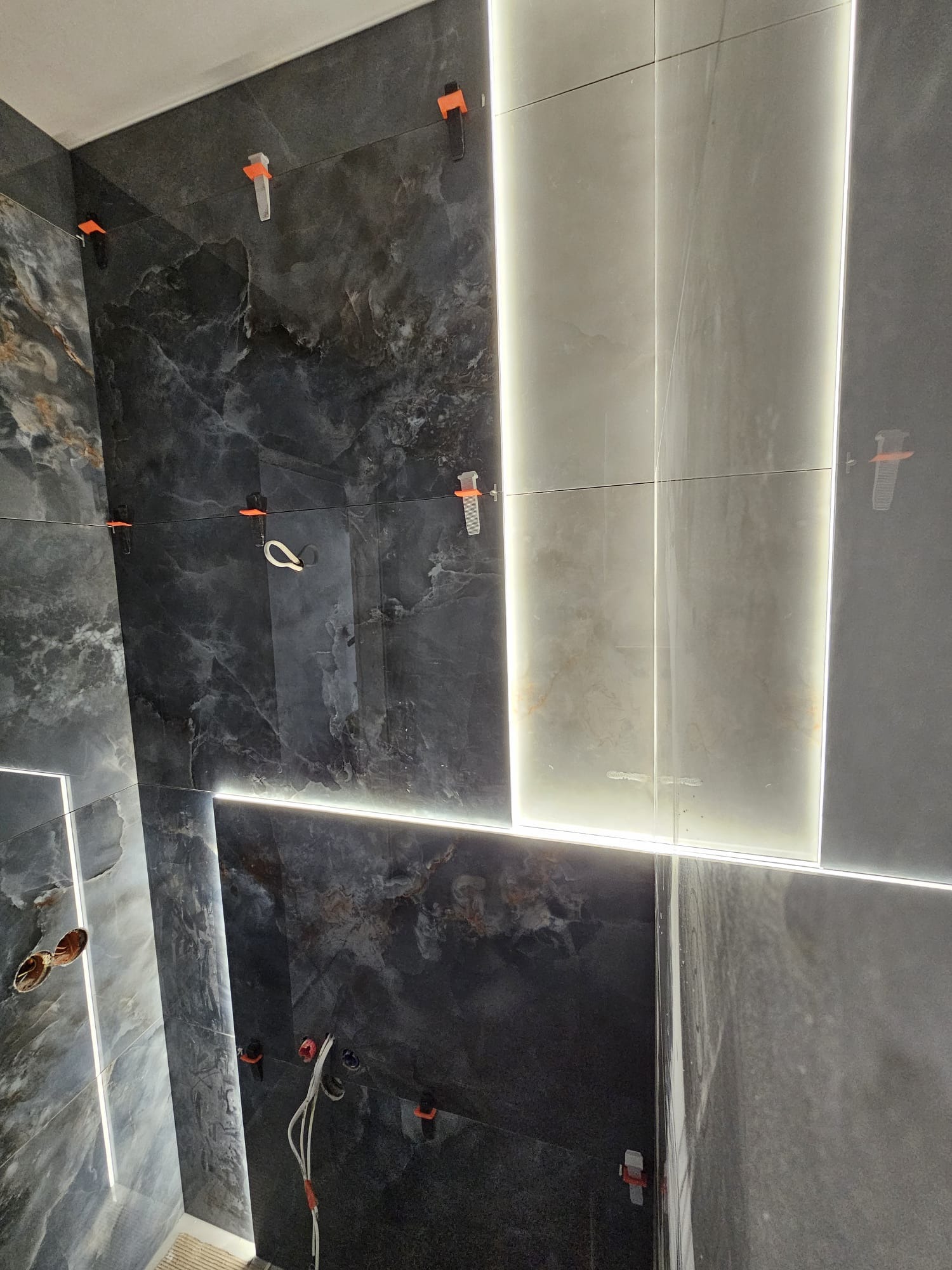 Ściana w trakcie układania płytek imitujących marmur, z podświetleniem LED w fugach i systemem poziomowania płytek.