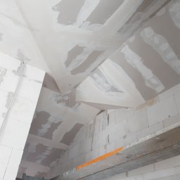 CNG-Uslugi Budowlane - Poddasze z surowymi ścianami i skośnym sufitem z płyt kartonowo-gipsowych w trakcie szpachlowania, widoczne rusztowanie i instalacja elektryczna.