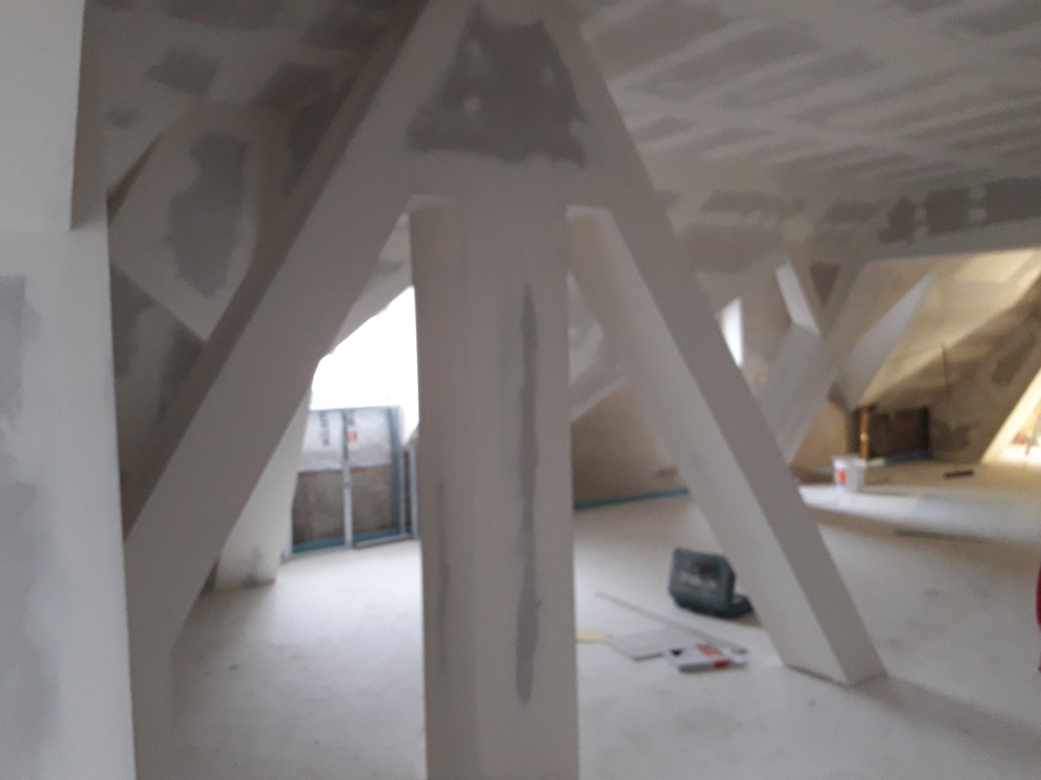 Poddasze w Skrzyszowie w trakcie wykańczania, widoczne białe, surowe słupy konstrukcyjne i płyty gipsowo-kartonowe na suficie, ślady szpachlowania.