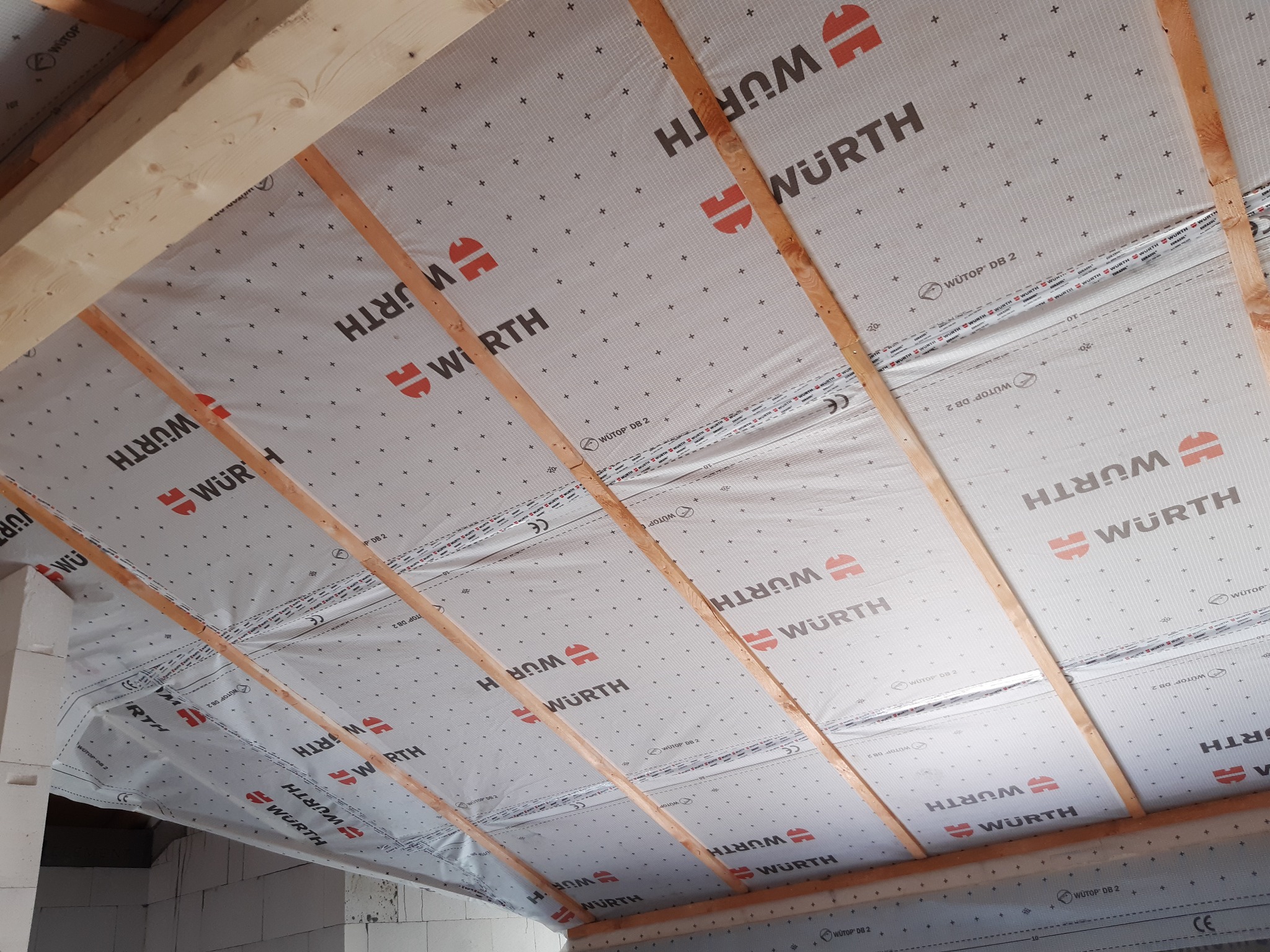 Izolacja poddasza z widocznymi krokwiami i membraną dachową z logo Wurth, widok od dołu.