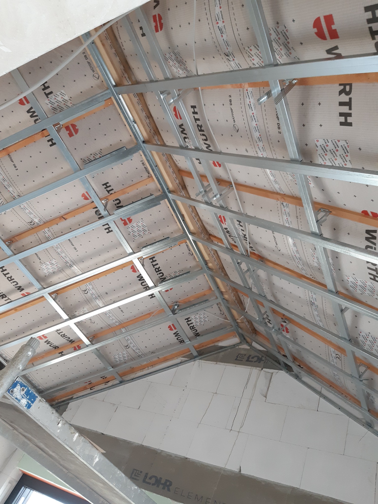 Konstrukcja poddasza z metalowym stelażem i membraną izolacyjną Wurth, widok z dołu, częściowo ocieplone ściany z białych bloczków.