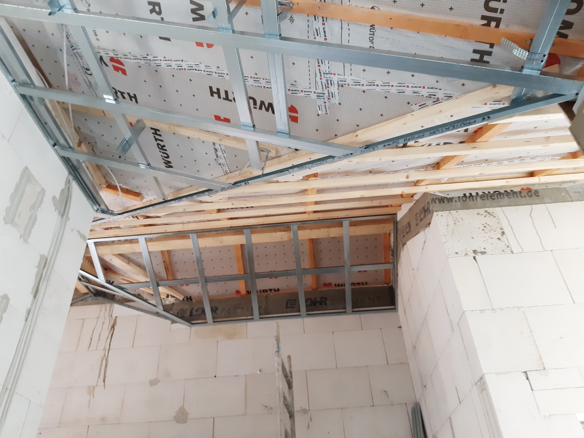 Konstrukcja metalowa pod płyty karton gips na poddaszu, widoczne drewniane belki i folia izolacyjna marki Wurth, ściany z białego betonu komórkowego.