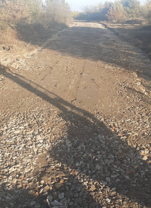 Utwardzanie drogi gruntowej: warstwa tłucznia i wyrównany teren. Długi cień na pierwszym planie. Widok na dalszą część drogi i drzewa.