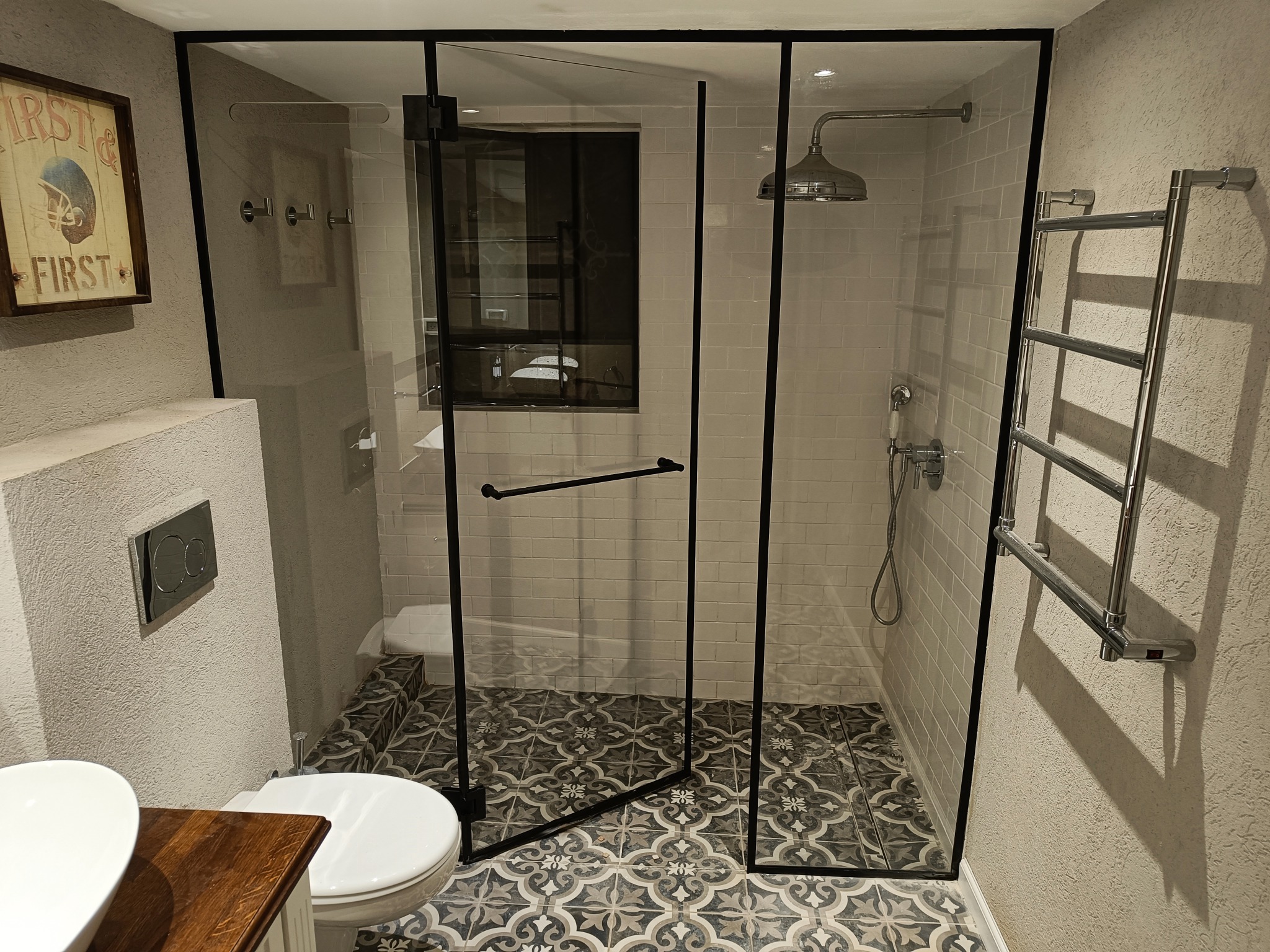 Nowoczesna kabina prysznicowa ze szklanymi drzwiami w czarnej ramie, widoczna armatura, grzejnik drabinkowy i dekoracyjna podłoga.