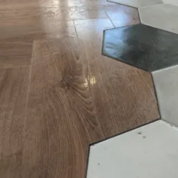 Połączenie paneli imitujących drewno z heksagonalnymi płytkami podłogowymi w Łapanowie, widok z bliska na łączenie materiałów.