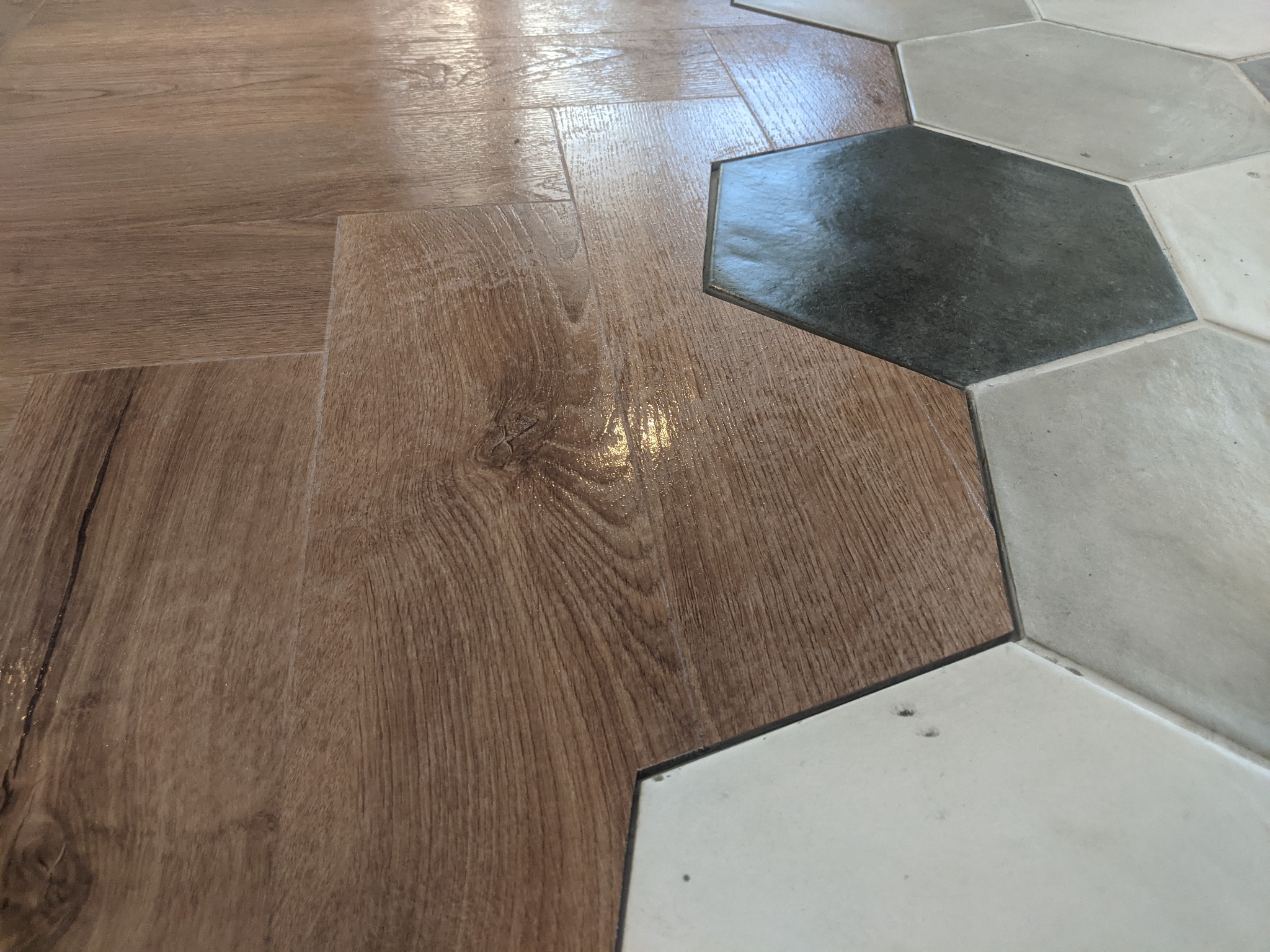 Połączenie paneli imitujących drewno z heksagonalnymi płytkami podłogowymi w Łapanowie, widok z bliska na łączenie materiałów.