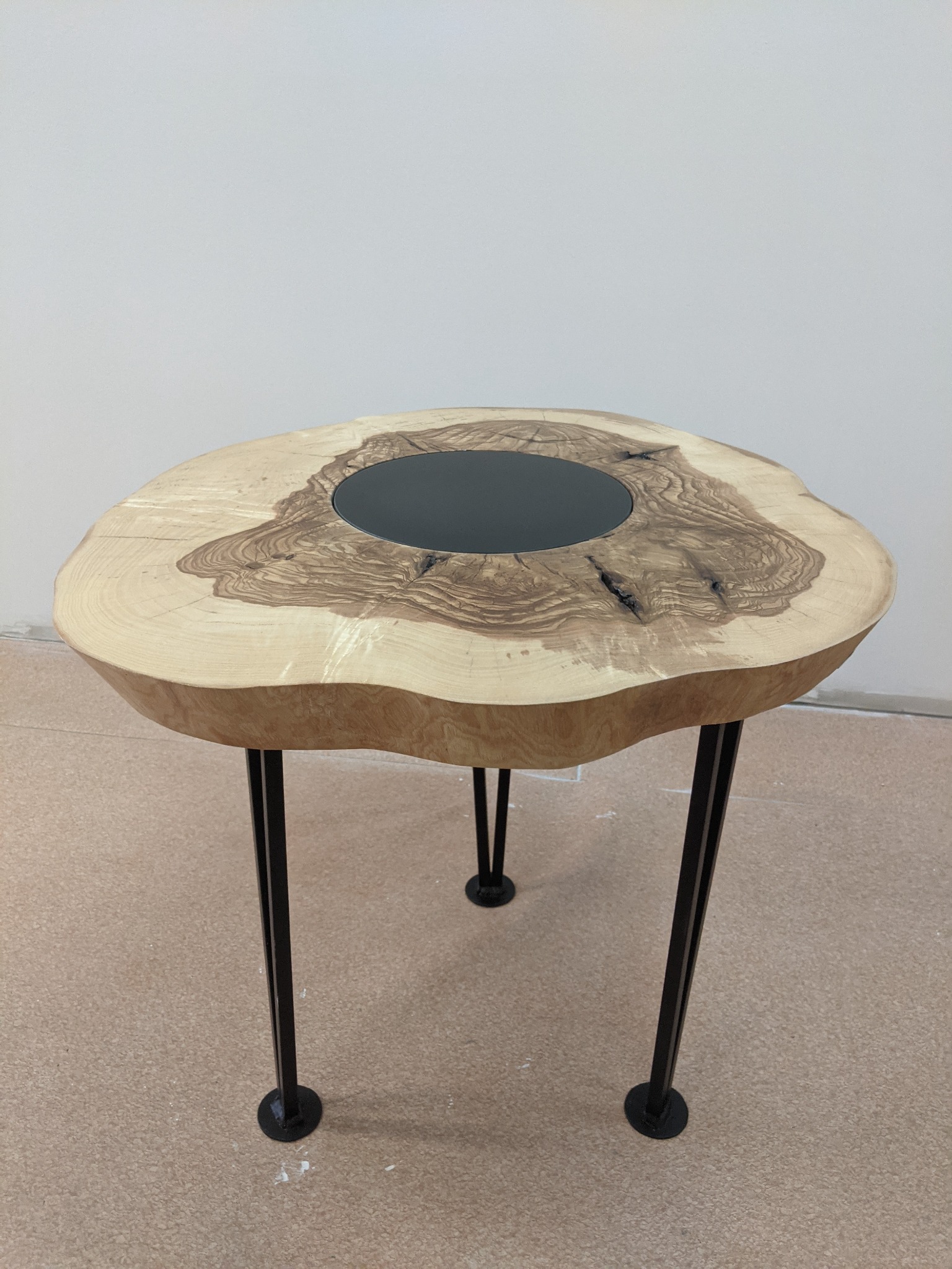 Okrągły stolik kawowy z blatem z plastra drewna z czarną żywicą epoksydową w środku i trzema metalowymi nogami.
