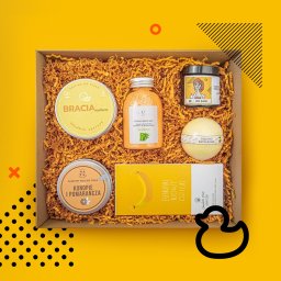Bartosz Dymek - Zestaw prezentowy z kosmetykami do pielęgnacji ciała w kartonowym pudełku wypełnionym siankiem: peeling, mus do ciała, sól do kąpieli, kula do kąpieli i czekolada z motywem banana.