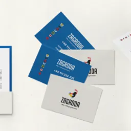 Zestaw wizytówek i materiałów firmowych z logo przedstawiającym kolorowego koguta i motywy ludowe, ułożonych na jasnym tle.