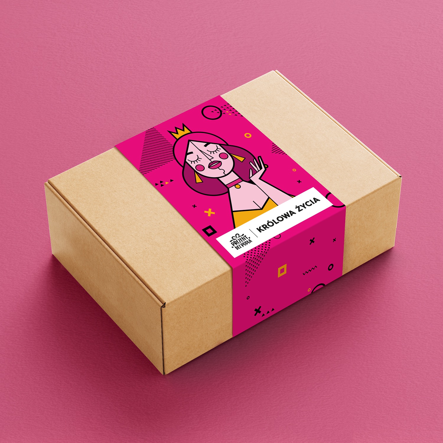 Kartonowe pudełko z różową opaską z ilustracją królowej i napisem 'Królowa Życia', leżące na różowym tle.