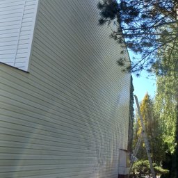 Clean Manager - Elewacja budynku z sidingu w Lublinie, widok z dołu. Obok drzewa i drabina oparta o ścianę. Jasne, naturalne światło słoneczne.