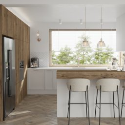 STUDIO OF3 - Jasna kuchnia z drewnianymi akcentami: wyspa z trzema hokerami, okno z widokiem na zieleń, lodówka side-by-side w zabudowie z forniru dębowego, podłoga w jodełkę.