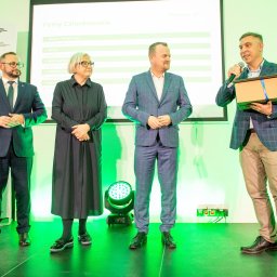 Smart Selling Group Dariusz Gawron - Prezentacja dla firm członkowskich Regionalnej Izby Gospodarczej: mężczyzna w garniturze wręcza nagrodę w pudełku podczas oficjalnego spotkania na scenie.