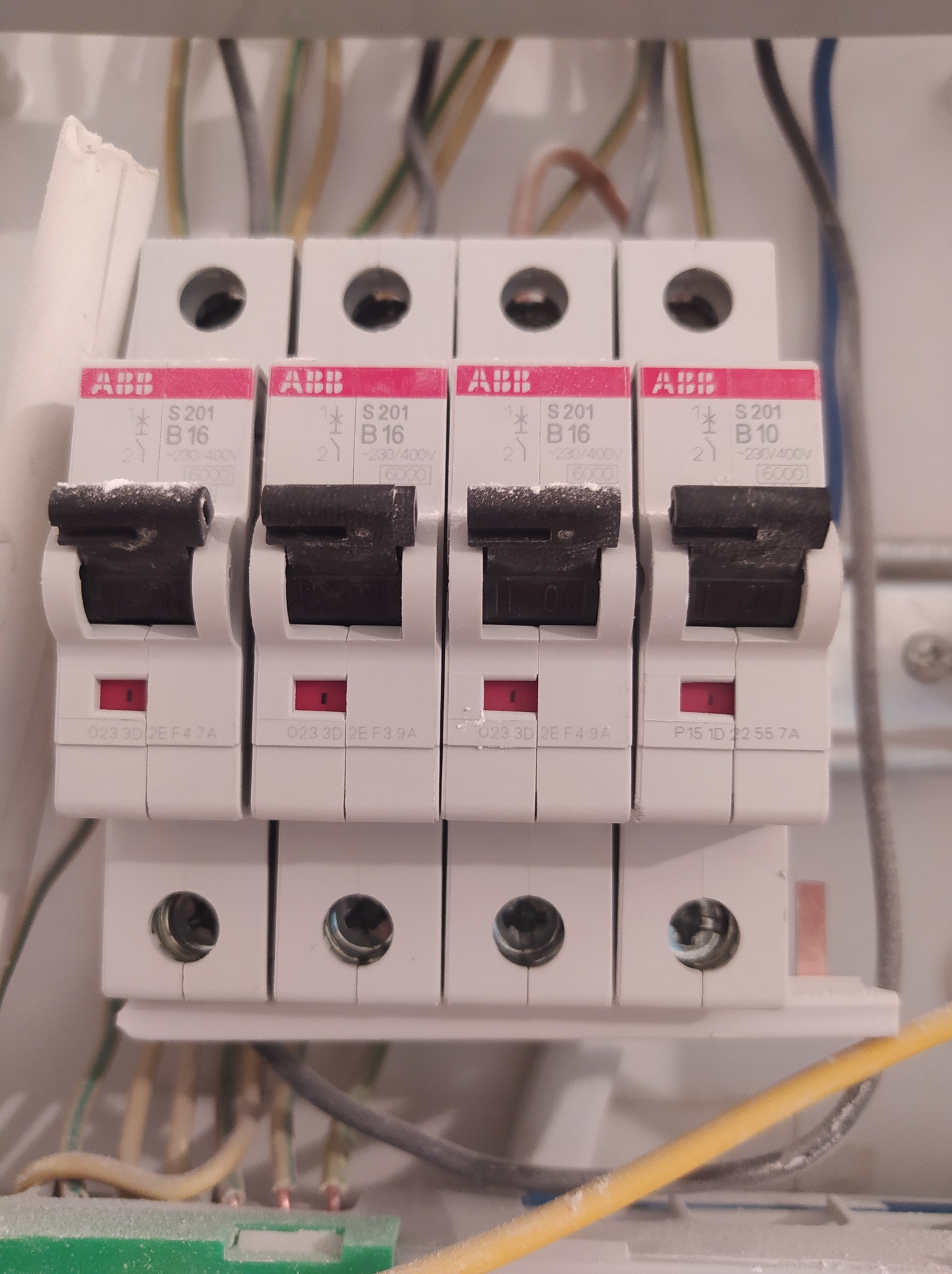 Cztery zabezpieczenia nadprądowe ABB S201 B16 i B10 zamontowane w rozdzielnicy, widoczne przewody zasilające, na obudowie osadził się kurz.