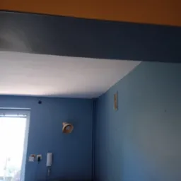 Pomieszczenie po odświeżeniu: błękitne ściany, biały sufit, z pomarańczowym pasem pod sufitem. Widoczne gniazdka, lampka i fragment mebli.