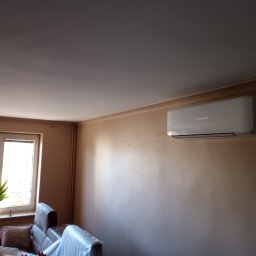 Lukas - Beżowa ściana w pokoju z zamontowanym klimatyzatorem Mitsubishi, zabezpieczone meble folią malarską.