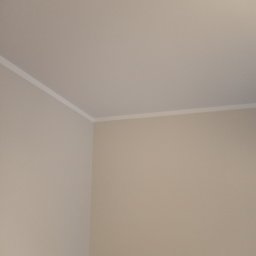 Lukas - Pomieszczenie po malowaniu ścian na jednolity, jasny beżowy kolor, z widoczną białą listwą przypodłogową przy suficie.