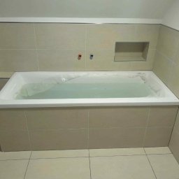 Lukas - Wykończona łazienka z wanną obłożoną beżowymi płytkami, widoczne baterie i wnęka w ścianie. Minimalistyczny design, jasne wnętrze.