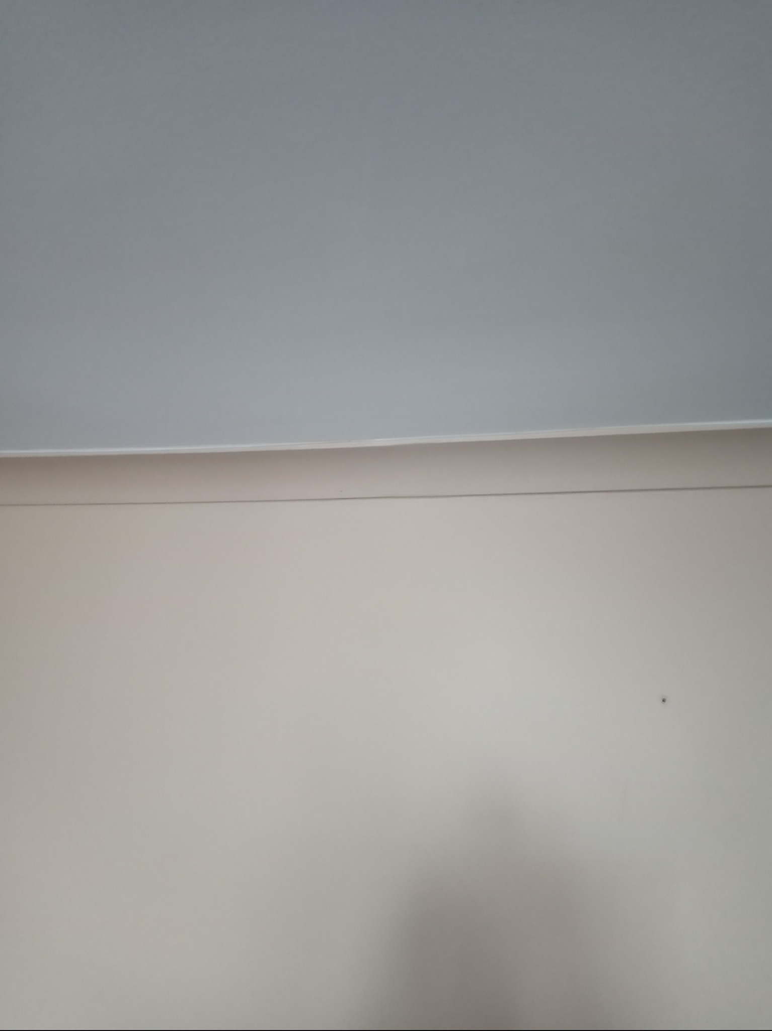 Świeżo pomalowana ściana w odcieniach beżu z białym sufitem, widoczny cień i mała plamka na ścianie.