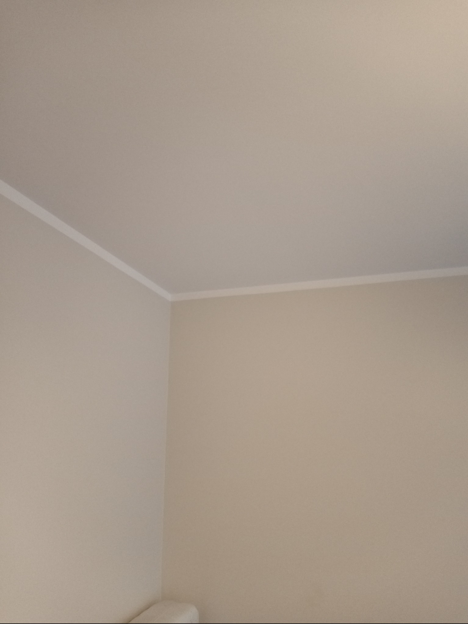 Pomieszczenie po malowaniu ścian na jednolity, jasny beżowy kolor, z widoczną białą listwą przypodłogową przy suficie.