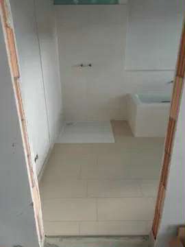 Jasne płytki podłogowe w łazience, widok z progu. Minimalistyczny design, świeżo położona podłoga, przygotowana do dalszych prac wykończeniowych.