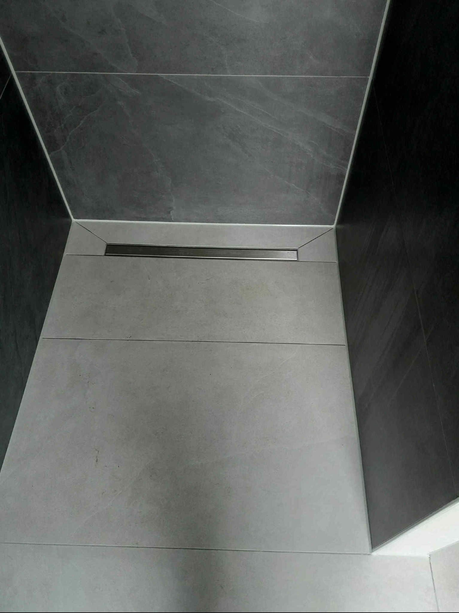 Nowoczesna kabina prysznicowa z szarymi płytkami imitującymi kamień i odpływem liniowym. Minimalistyczny design, precyzyjne ułożenie płytek.