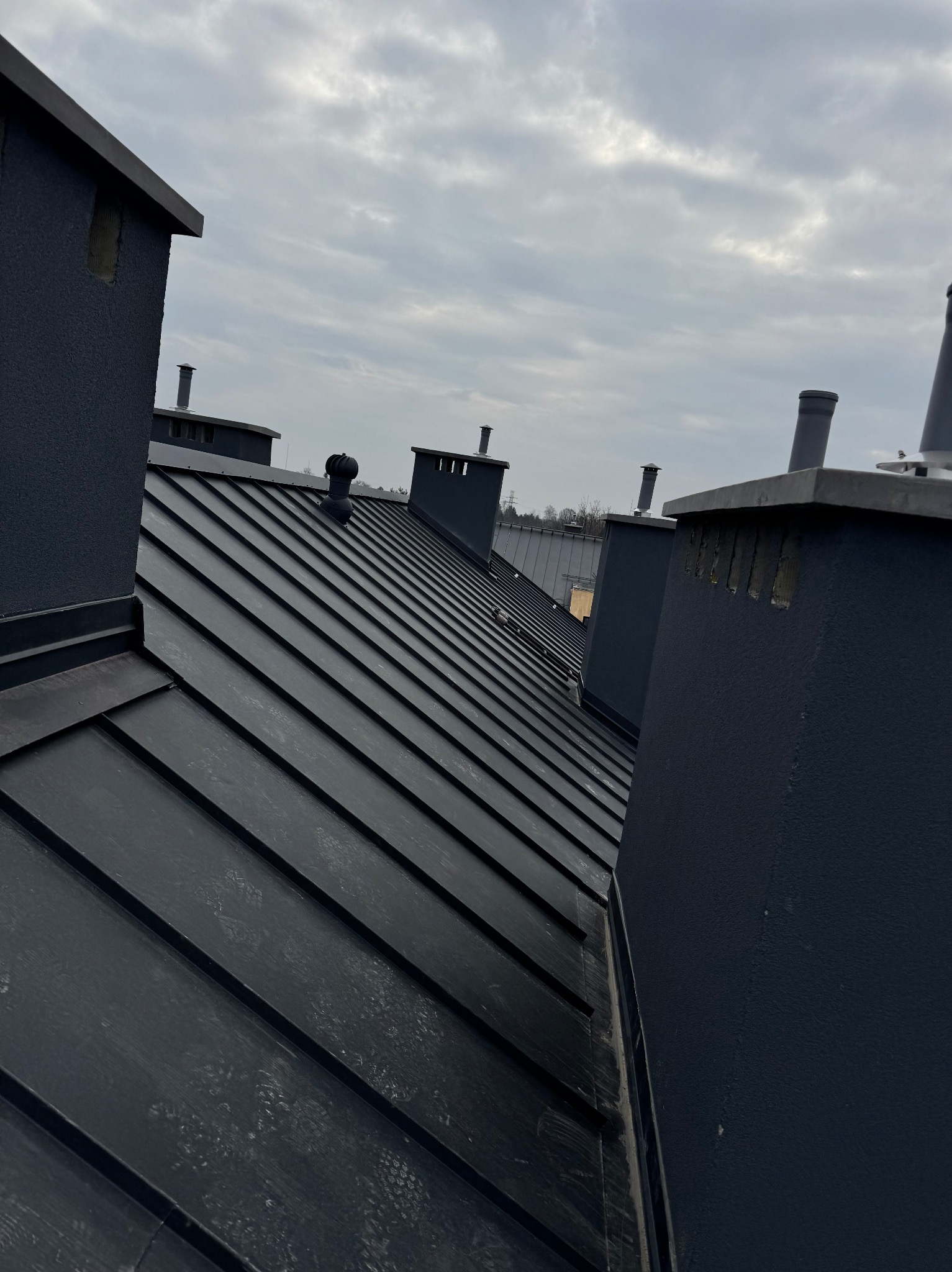 Nowy, czarny dach z blachy na budynku z kominami, widok z góry w pochmurny dzień.