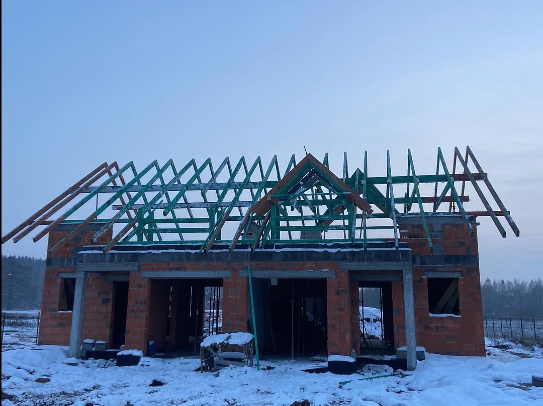 Surowy stan budynku z cegły z częściowo ukończoną, zieloną konstrukcją drewnianą dachu w zimowym krajobrazie.