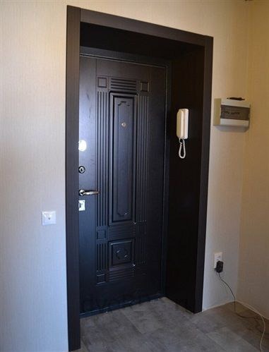 Czarna, metalowa, ozdobna drzwi wejściowe z brązową ościeżnicą, widok od wewnątrz, na ścianie domofon i skrzynka na listy.