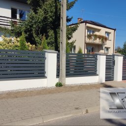 Szczygielski-Ogrodzenia - Nowoczesne ogrodzenie z poziomych, szarych paneli zamontowane na białych słupkach, z bramą wjazdową w tle, na tle dwóch domów i słupa energetycznego.