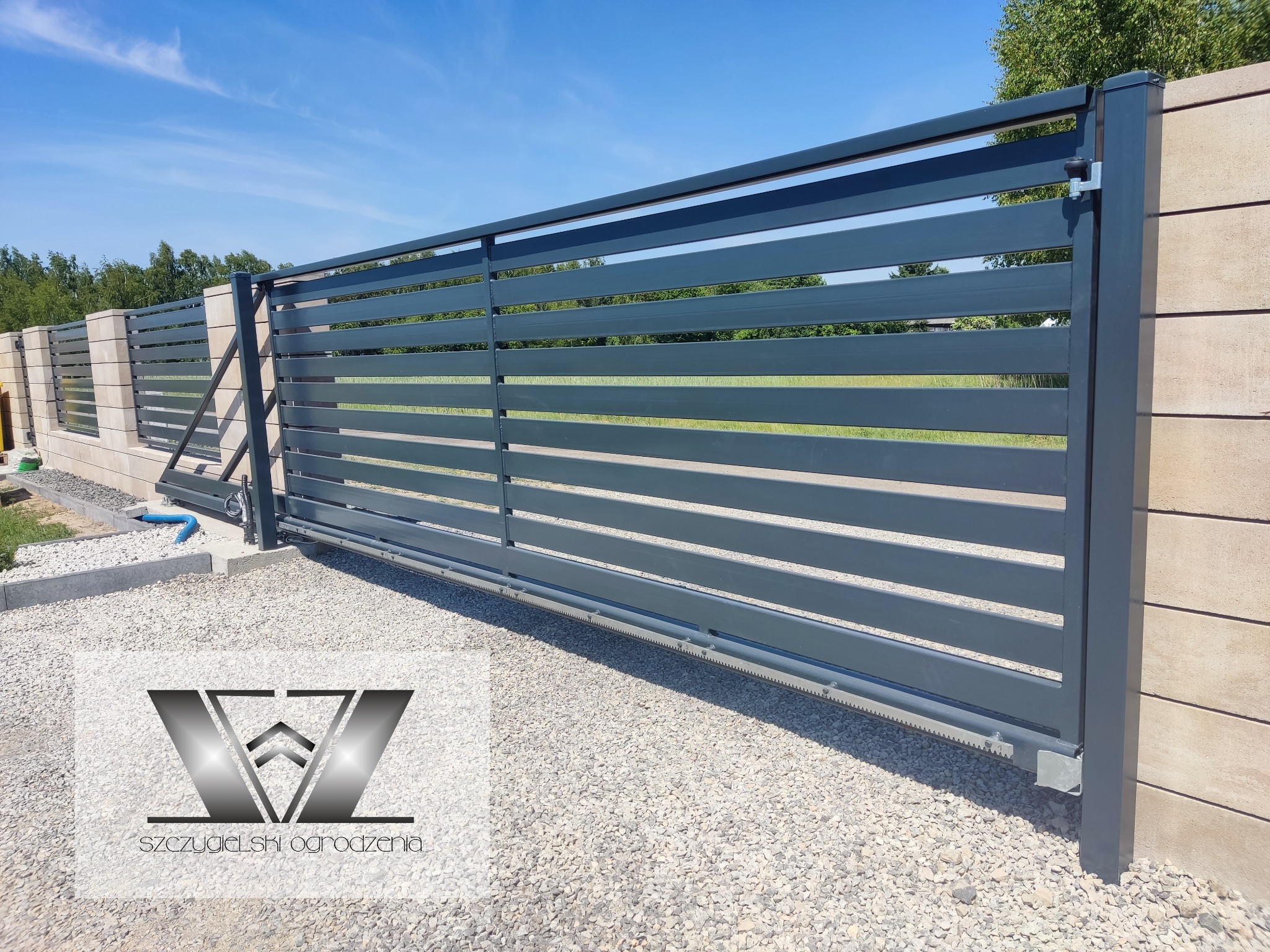 Nowoczesna, przesuwna brama wjazdowa z poziomych profili, zamontowana w Parczewie, widoczna na tle jasnego nieba i kamiennego podłoża.